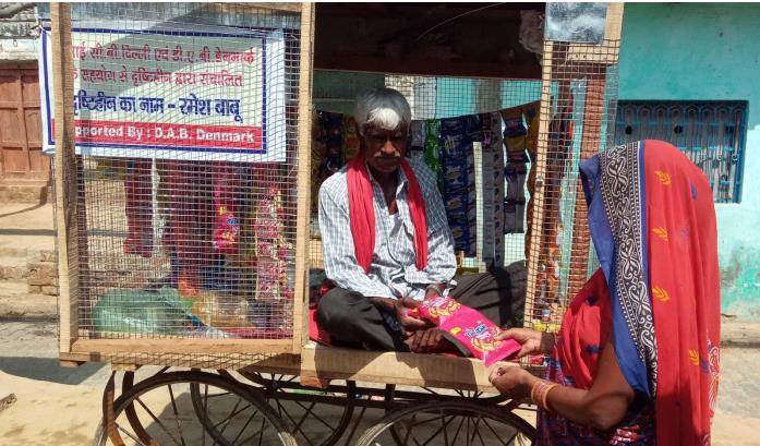 Ramesh Babu selling goods to a woman from his mobile petty shop